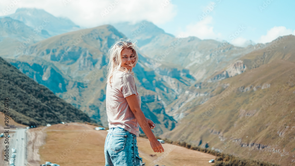 Naklejka premium Woman hiking in mountains at sunny day time. View of Kazbegi, Georgia. Beautiful natural mountain background