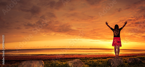 Frau mit rotem Rock geniesst den Sonnenuntergang am Meer