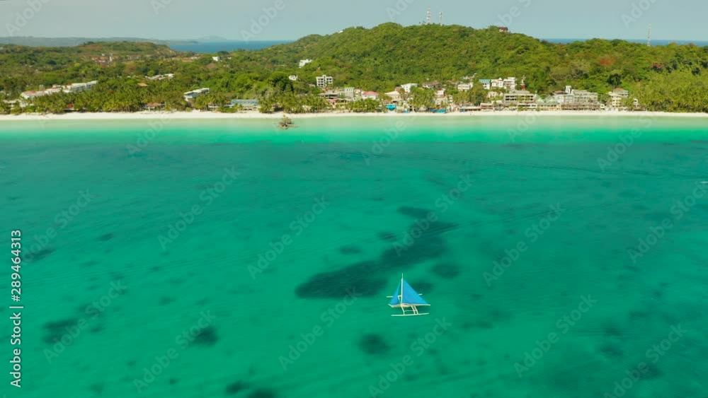 Sailing yacht in crystal clear turquoise water right next to the white sand beach of tropical island, aerial view. Sailing boat glides over the waves, Boracay, Philippines. Sailing yacht in crystal clear turquoise water right next to the white sand beach of tropical island, aerial view. Sailing boat glides over the waves, Boracay, Philippines.