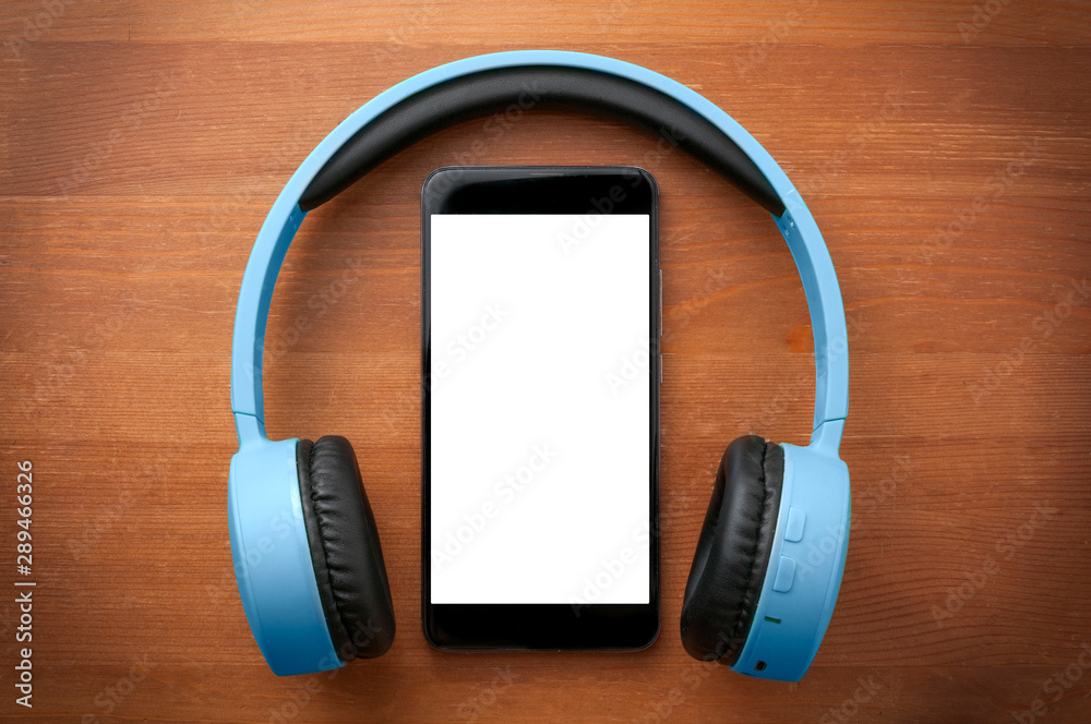 Pair of blue headphones around a blank screen smartphone on orange wooden table