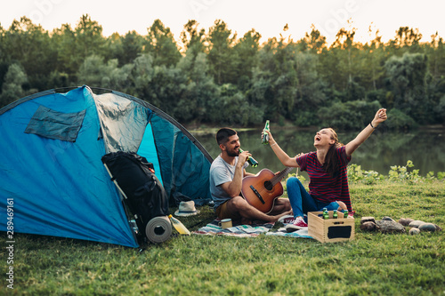couple on camping , playing guitar and drinking beer , by the lake