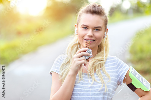 Athletic sporty woman eating energy bar after jogging in park
