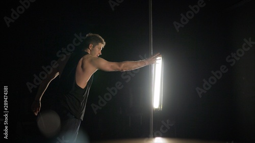 The guy shows the exercise on a pole.. Male pole dance. Photo of muscular man posing