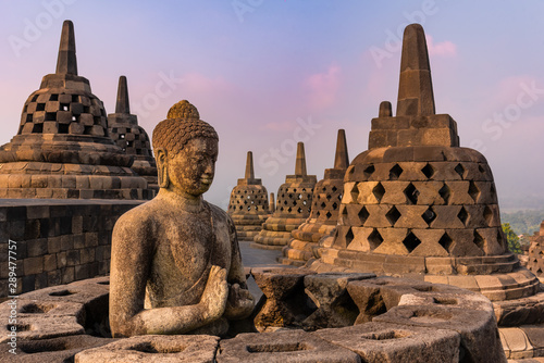 Breathtaking view of the sunrise from the meditating Buddha statue and stone stupas against a bright sun background. The ancient Buddhist temple of Borobudur. Great religious architecture. Magelang,