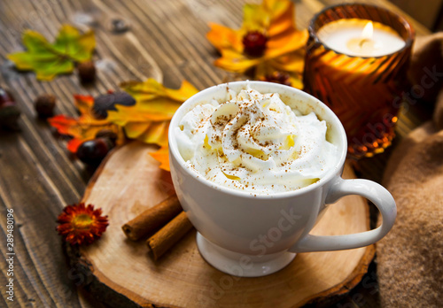 Spicy pumpkin latte with whipped cream. Autumn coffee cup with pumpkin and cinnamon spice on wooden table with fall candle and decoration still life