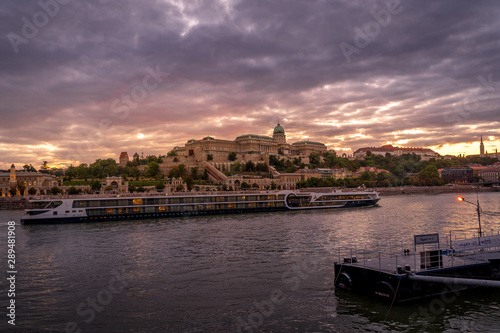 Buda castle with a river cruise passing by on the Danube with dramatic sunset sky