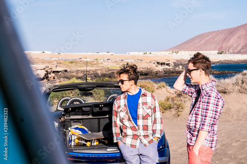 couple of teenagers smiling and have fun together at the beach, surfer boy and surf - surfing - 20s with glasses and sunglasses outdoor wait to go to surf with sea at the background