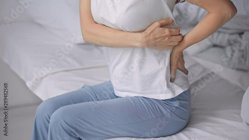 cropped view of woman sitting on bed with backache
