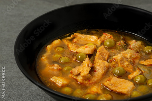 Belly pork or streaky pork in spicy curry soup with turkey berry in black bowl on tile table.