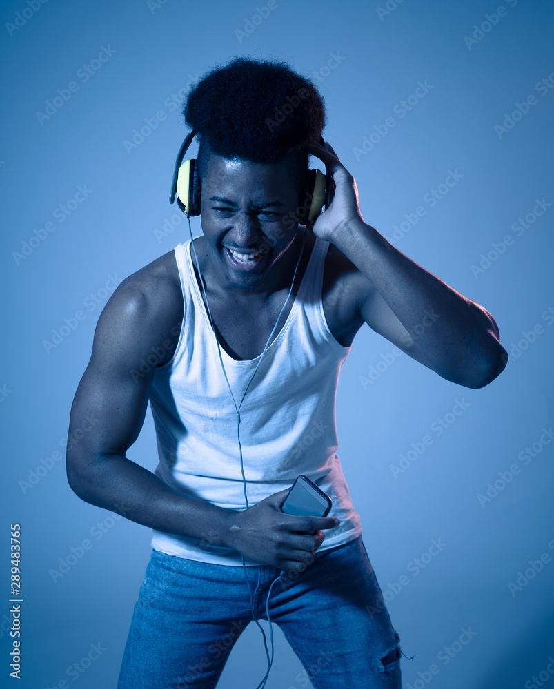 Attractive young african american man with headphones dancing and singing to music on mobile in disco light