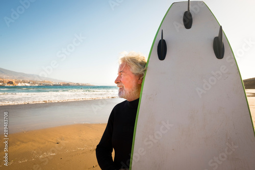 Photography happy senior with surftable and black wetsuit a at the beach si looking at the s
