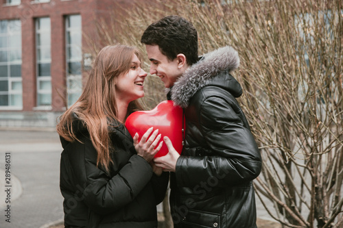 A cute couple of young people in love holding a red ball in the shape of a heart, hugging each other and experiencing tender feelings, Valentine's Day