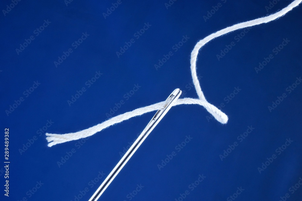 Needle sewing pointed tool and thread threaded into the eye of the needle. Designed for stitching clothing items. Background for design, sewing, needlework, creativity.