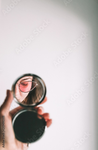 Girl in pink sunglasses looks in the mirror on white background. Modern and minimal fashion concept. Reflection beauty woman