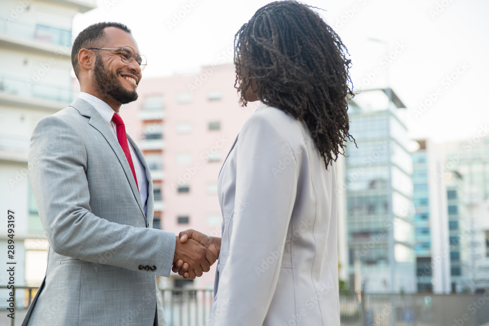 Friendly diverse business colleagues glad to see each other. Business man and woman standing outside and shaking hands. Corporate meeting concept Friendly diverse business colleagues glad to see each other. Business man and woman standing outside and shaking hands. Corporate meeting concept