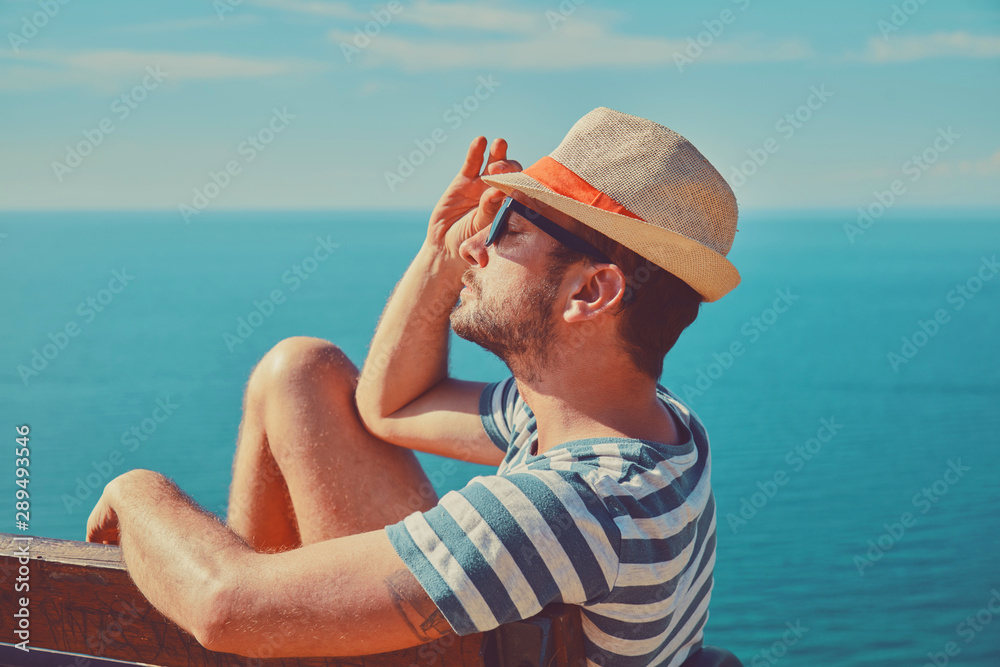Attractive man sitting on the bench and enjoying on the tropical beach. Summer concept.