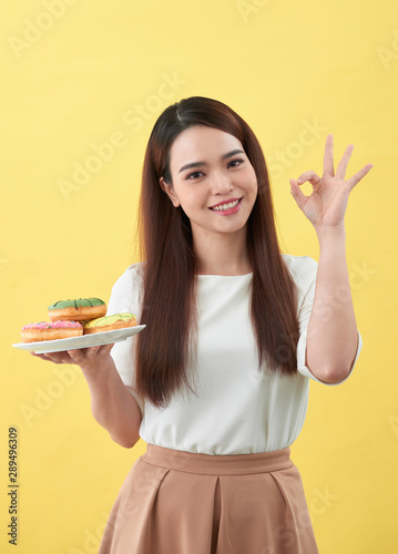Beautiful young woman smiling holding a plate full of delicious color donuts