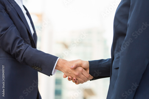 Female business partners meeting outside. Business women in office suits standing and shaking hands. Collaboration concept © Mangostar