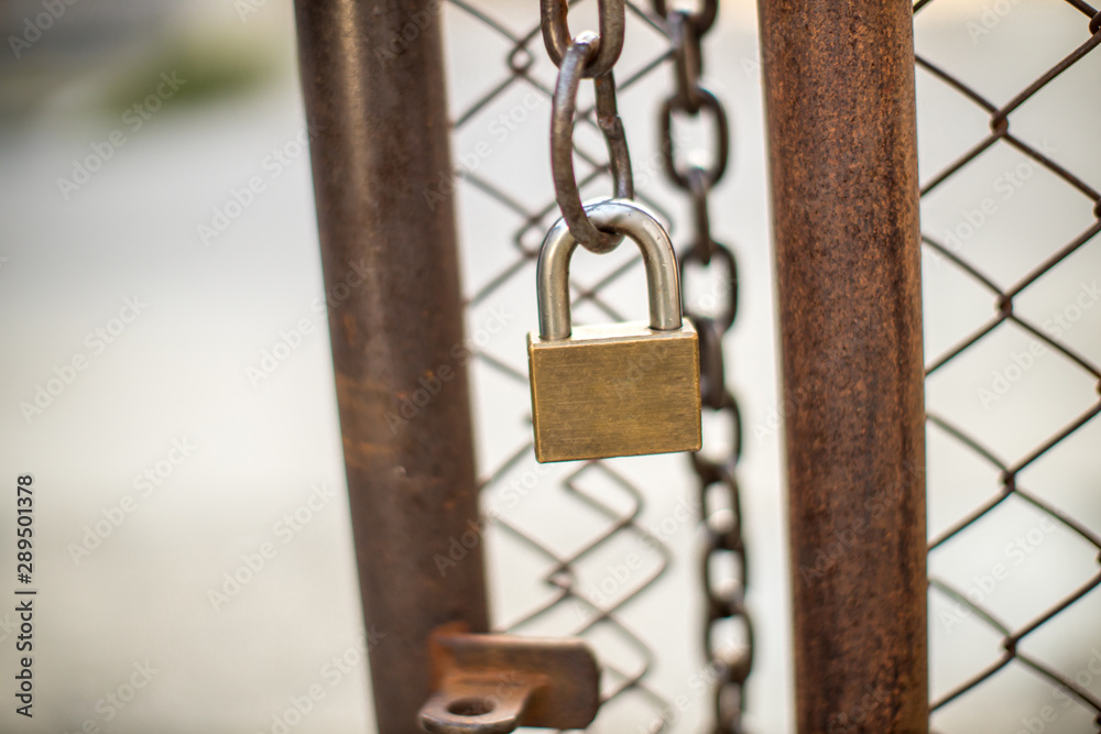 Lock on a chain link security fence. Chicken wire fence gate is locked with a chain and a padlock. padlock and strong steel chain wrapped around the metal entrance gate. Lock on a chain link security fence. Chicken wire fence gate is locked with a chain and a padlock. padlock and strong steel chain wrapped around the metal entrance gate.