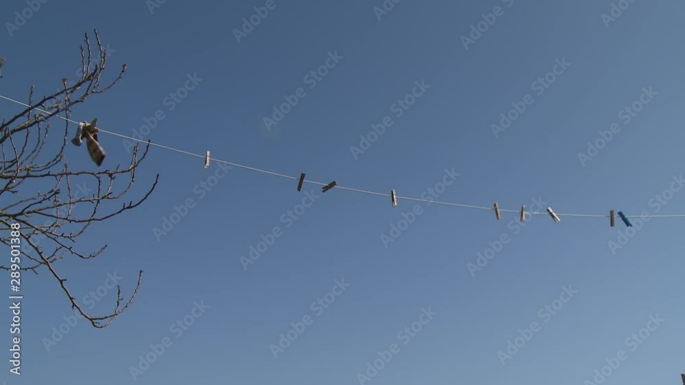 Wide low angle shot of empty clothes pins and a single sock drying on a clothesline with a clear blue sky behind Wide low angle shot of empty clothes pins and a single sock drying on a clothesline with a clear blue sky behind