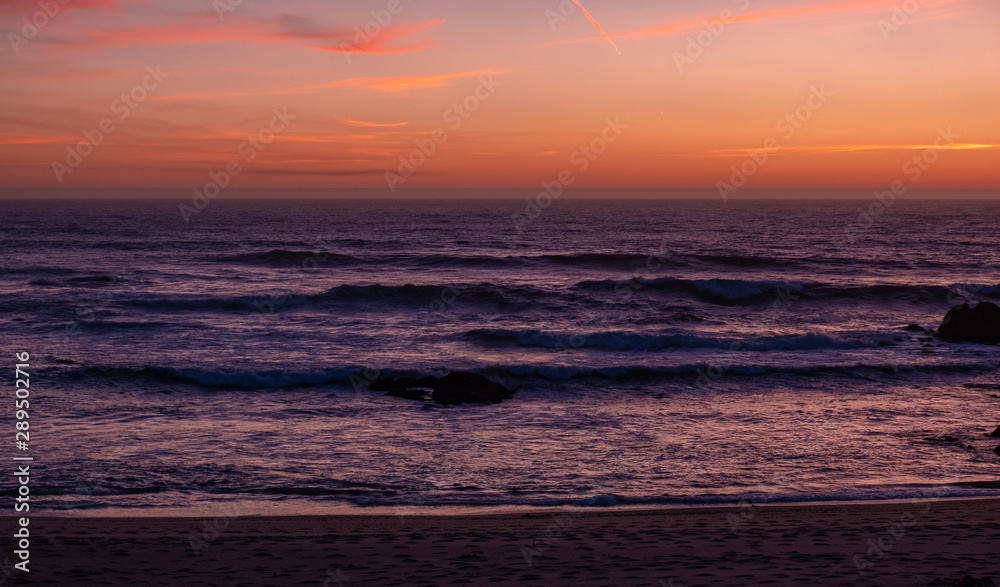 Beautiful dusk over ocean with dark purple waves and orange red sky