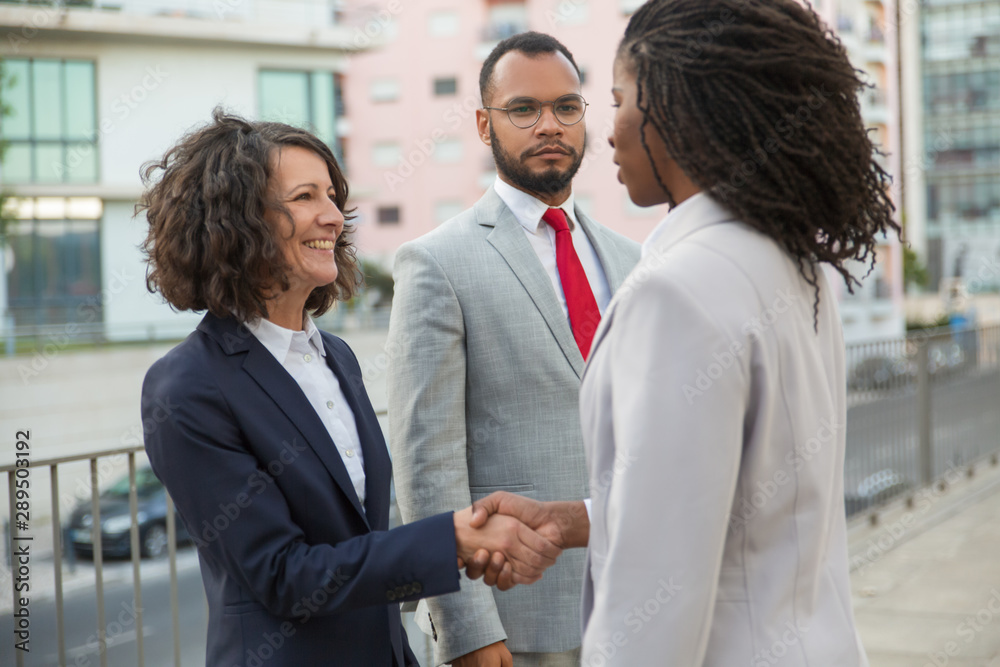 Consultant and customers meeting outside. Business man and women standing near city building and shaking hands. Diverse partners concept Consultant and customers meeting outside. Business man and women standing near city building and shaking hands. Diverse partners concept