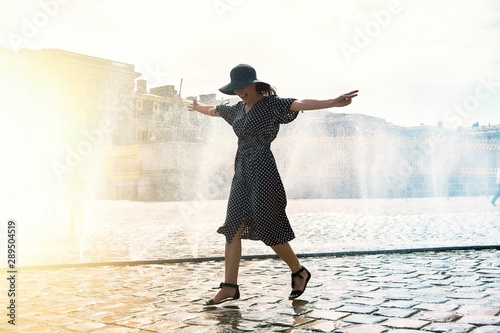 Happy girl in dress and hat in a spray of water on a sunny summer day  Versailles  France