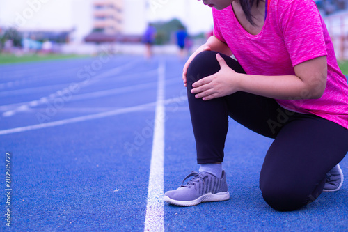 Knee Injuries. Young sport woman holding knee with her hands in pain after suffering muscle injury during a running workout on Running Track. Healthcare and sport concept.