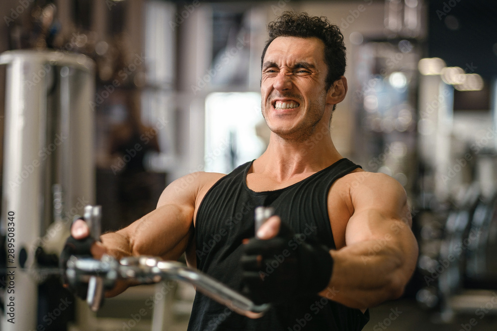 Man lifting weights at the cable machine in a gym. Lifting heavy weights and fatigue. Sport fitness and muscles concept Man lifting weights at the cable machine in a gym. Lifting heavy weights and fatigue. Sport fitness and muscles concept