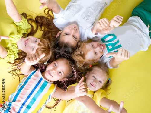 A group of fashionable children lie on a yellow background looking at the camera with their thumb up. Childhood, happy children