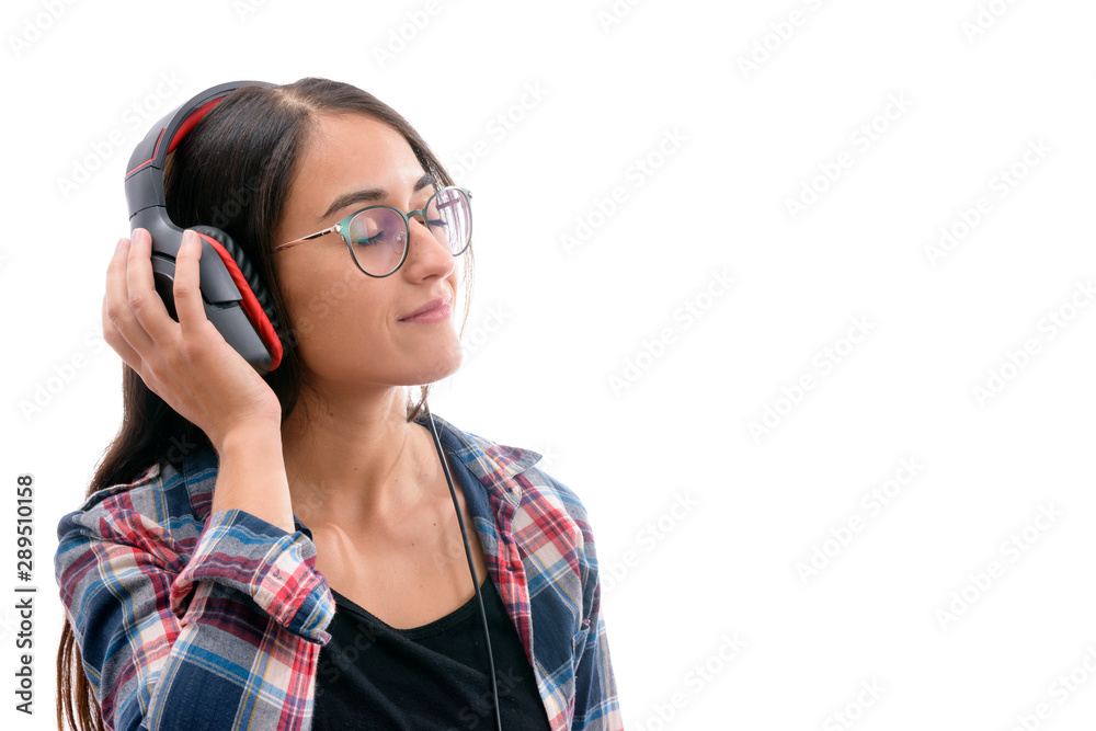 Caucasian young girl with plaid shirt and glasses, listening to music with big headphones and a mobile phone or other type of electronic device on white background isolated Caucasian young girl with plaid shirt and glasses, listening to music with big headphones and a mobile phone or other type of electronic device on white background isolated