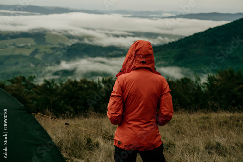 Back view of girl tourist in orange jacket looking at beautiful scenery of mountains © Daria