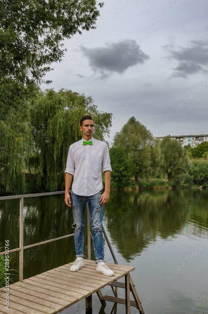 young man with a green bow-tie on a bridge on a lake background young man with a green bow-tie on a bridge on a lake background