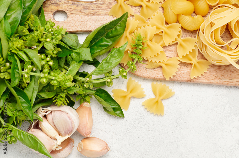 Different types of Italian pasta, fresh basil and garlic on wooden cutting board