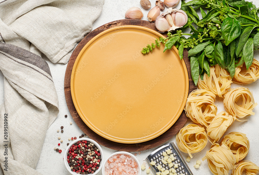 Yellow plate surrounded by different types of Italian pasta, fresh basil, garlic and mozzarella cheese
