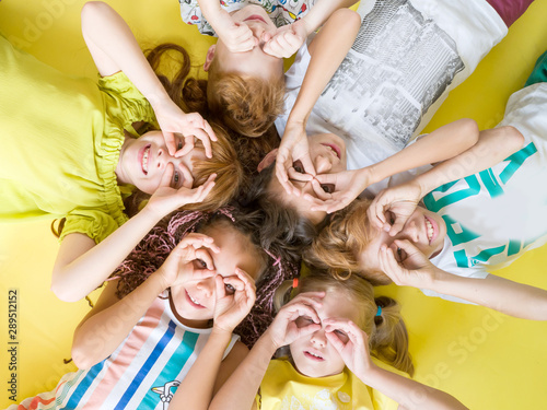 A group of fashionable children lie on a yellow background looking at the camera holding their hands to their eyes. Childhood, happy children