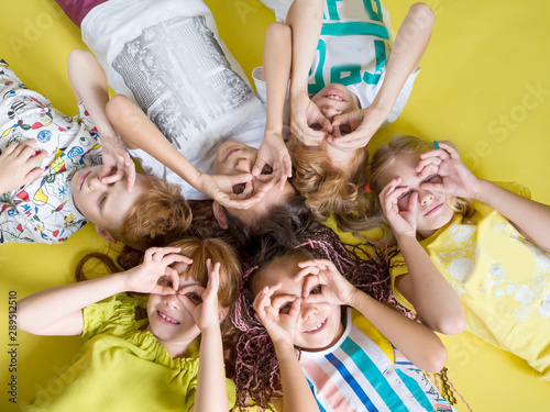 Group of joyful happy children lie on a yellow background looking at the camera. Fashion kids