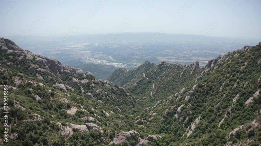 Drone shot of rocky mountain gorge covered with forest greenery and cityscape on horizon. Beautiful nature of Catalonia mountains, green plants, rocks, gorge, amazing landscape, Spain, Europe Drone shot of rocky mountain gorge covered with forest greenery and cityscape on horizon. Beautiful nature of Catalonia mountains, green plants, rocks, gorge, amazing landscape, Spain, Europe