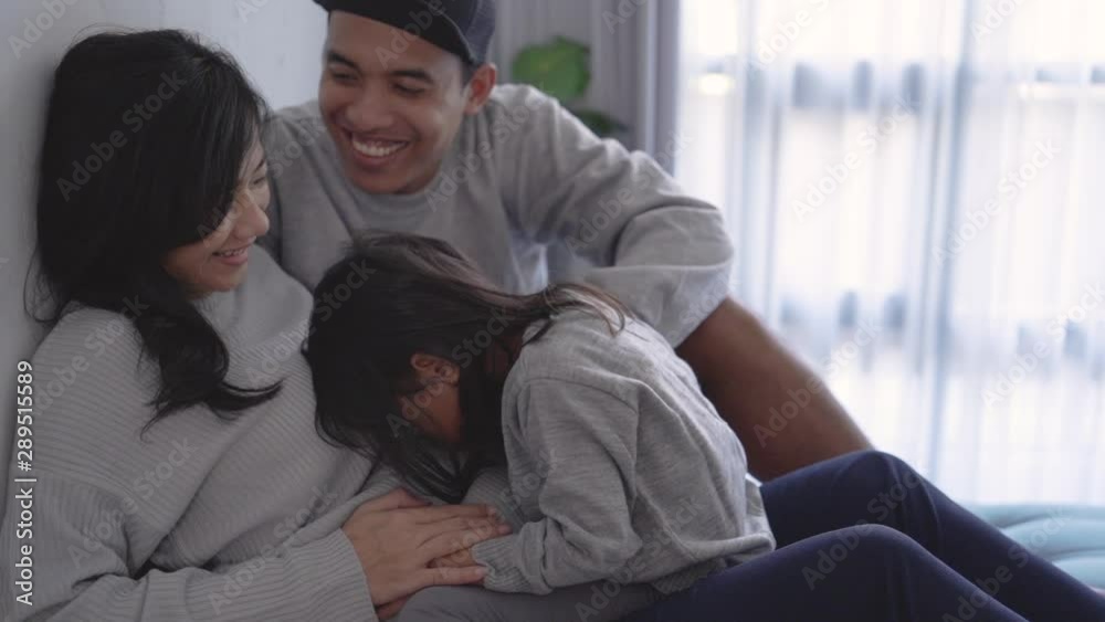 family togetherness, little girl with pregnant mother and father, joking together at leisure when sitting relaxed at home family togetherness, little girl with pregnant mother and father, joking together at leisure when sitting relaxed at home