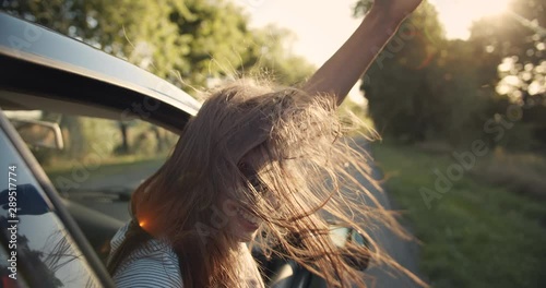 Happy young lady in eyeglasses looking out of car window and enjoying ride, wind fluttering hair, joy