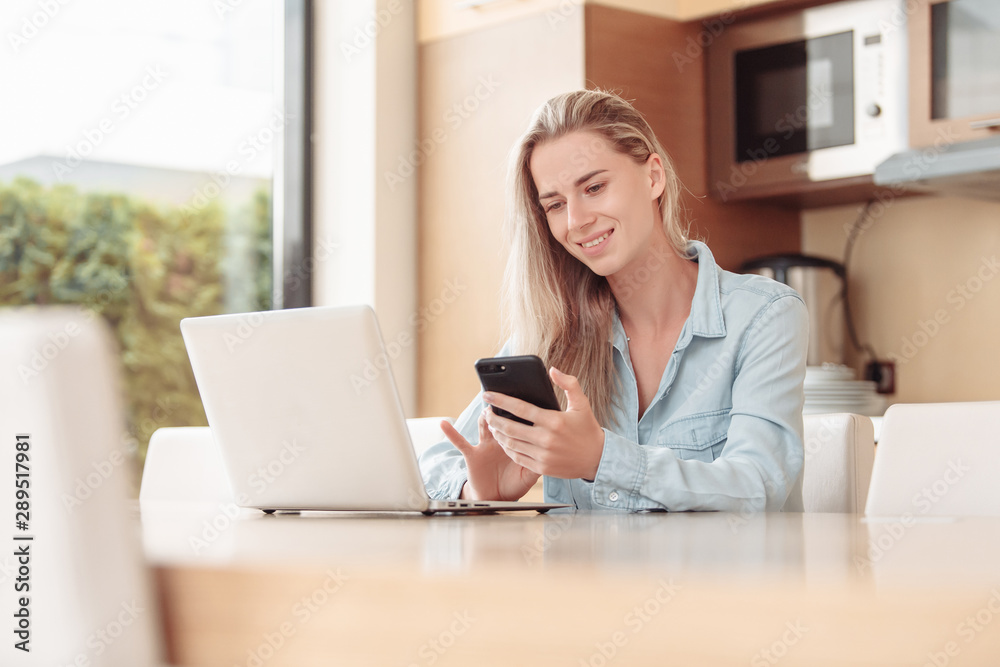 Smiling pretty young woman meets morning in the kitchen and checks mail using a laptop and high speed internet. Young woman freelancer has completed her job and is celebrating a new day Smiling pretty young woman meets morning in the kitchen and checks mail using a laptop and high speed internet. Young woman freelancer has completed her job and is celebrating a new day
