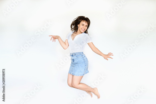 close up photo of a happy brunette in white blouse and denim skirt jumping in the air
