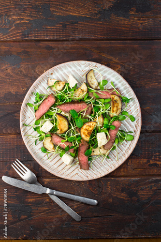 Green salad with steak, aubergine, sunflower sprouds and feta chese in ceramic plate on wooden background photo