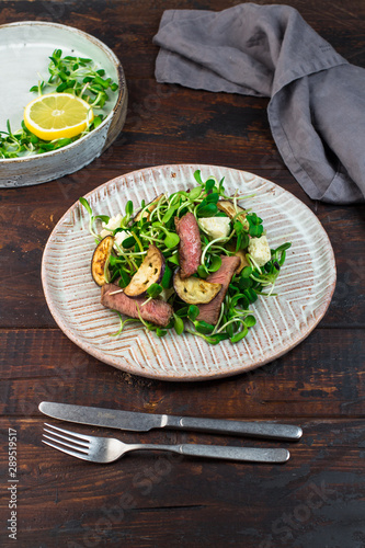 Green salad with steak, aubergine, sunflower sprouds and feta chese in ceramic plate on wooden background photo