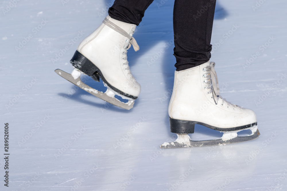 Ice skating, woman legs wearing white leather skates, training on a frosen snowy skating rink in winter close up Ice skating, woman legs wearing white leather skates, training on a frosen snowy skating rink in winter close up
