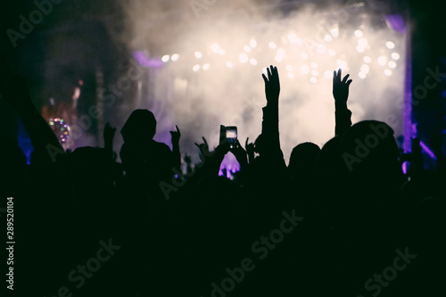 Silhouettes of raised hands on the concert in the night. The crowd of people at the open air music festival. Shooting a concert on the smartphone. Music background.
