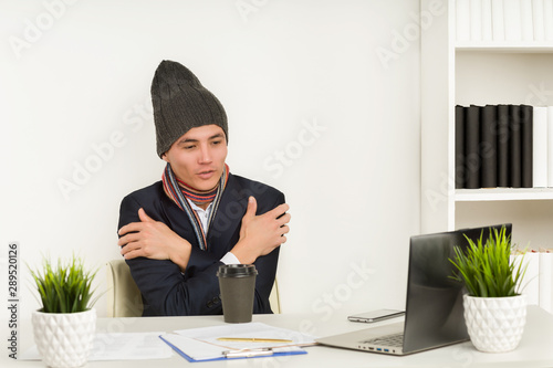 Tablou canvas Asian man in a hat, scarf and jacket freezes in office since broken heating or c