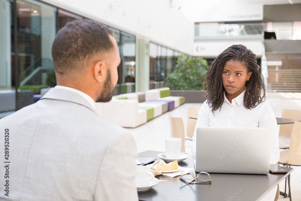 Young African American office employee having lunch with colleague. Business man and woman sitting at table in cafe, using laptop and talking. Corporate communication concept Young African American office employee having lunch with colleague. Business man and woman sitting at table in cafe, using laptop and talking. Corporate communication concept