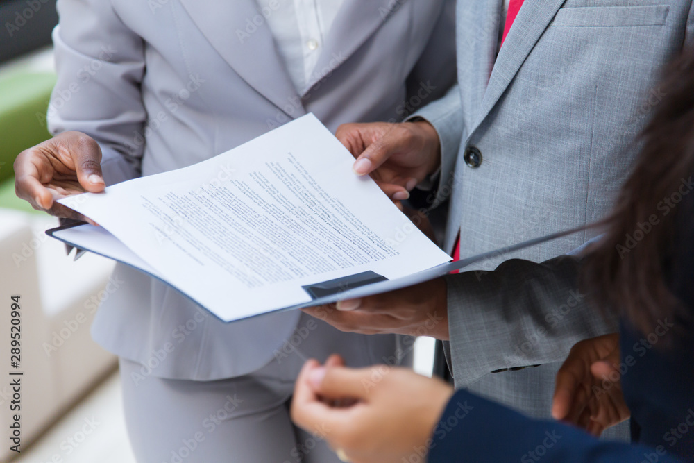Cropped shot of business colleagues with folder. Mid section of business people standing together and looking at papers in folder. Teamwork concept Cropped shot of business colleagues with folder. Mid section of business people standing together and looking at papers in folder. Teamwork concept