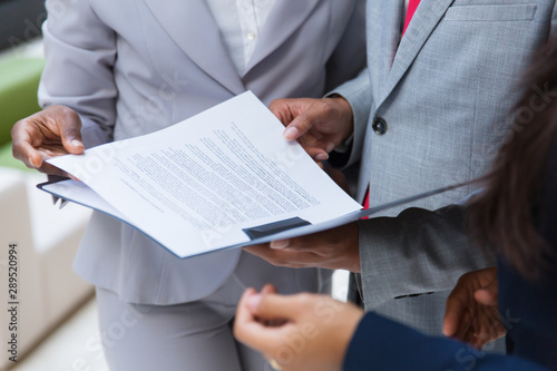 Cropped shot of business colleagues with folder. Mid section of business people standing together and looking at papers in folder. Teamwork concept